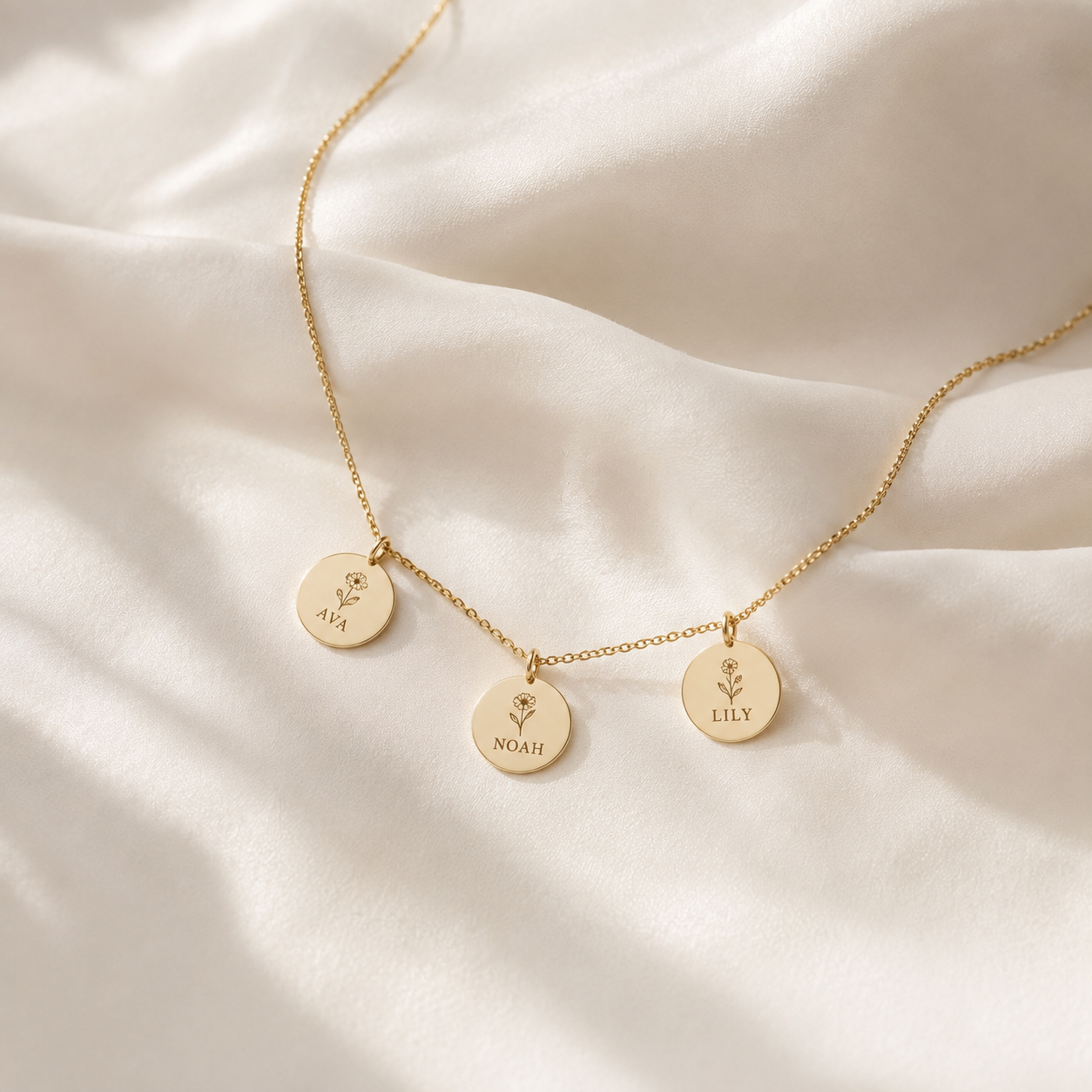 Gold necklace with three engraved name pendants on cream silk