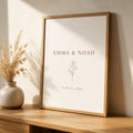 A framed anniversary print with two names and a date, leaning against a cream wall on an oak console
