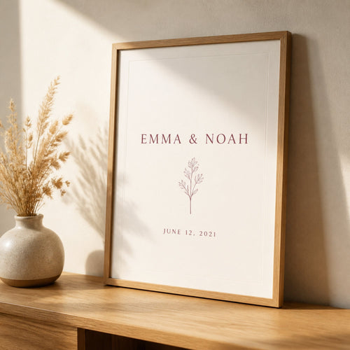 A framed anniversary print with two names and a date, leaning against a cream wall on an oak console