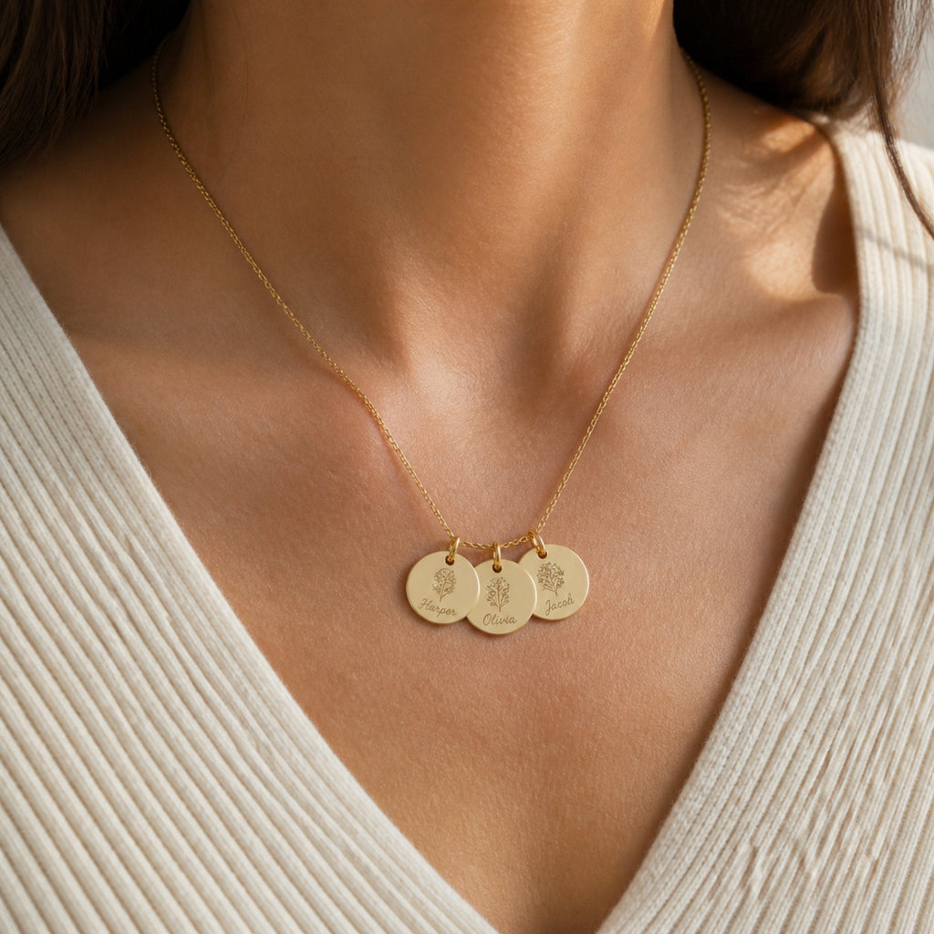 A gold three-disc engraved name necklace worn against a cream ribbed knit top