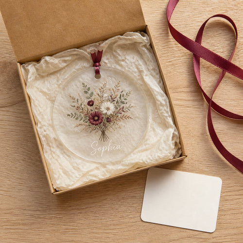 An open kraft gift box lined with cream tissue holding a personalized acrylic ornament
