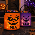 Orange and purple illuminated personalized Halloween treat baskets with candy and sample names MIA and LEO